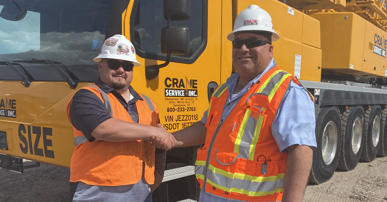 Two Crane Service Inc. team members shaking hands in front of a Liebherr crane