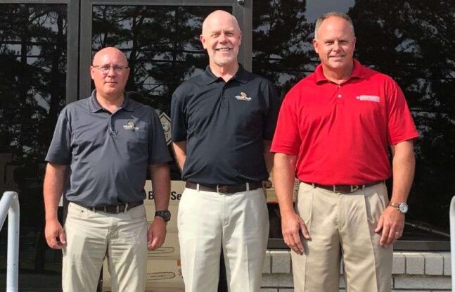 Mark McCarty, Tom Ficklin, and Darrin Brown in front of glass door announcing McClung-Logan's acquisition of White Oak Equipment