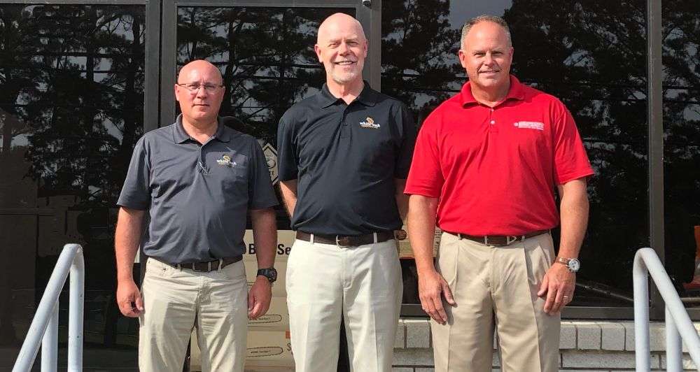 Mark McCarty, Tom Ficklin, and Darrin Brown in front of glass door announcing McClung-Logan's acquisition of White Oak Equipment